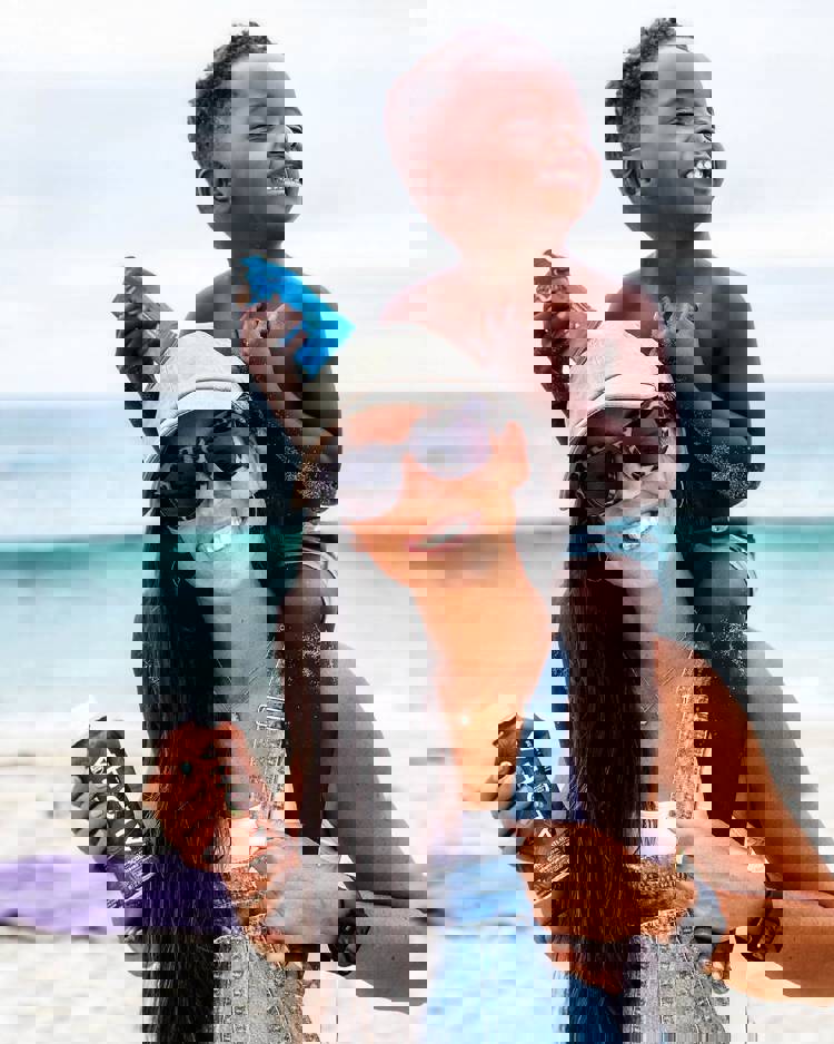 a woman is carrying a child on her shoulders on the beach while holding a bottle of aloha