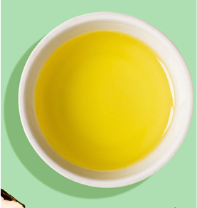 White bowl filled with yellow liquid on a green background.