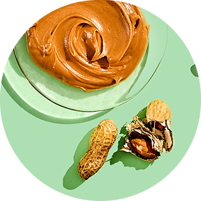 Peanut butter swirl on a plate with whole and cracked peanuts on a green background.